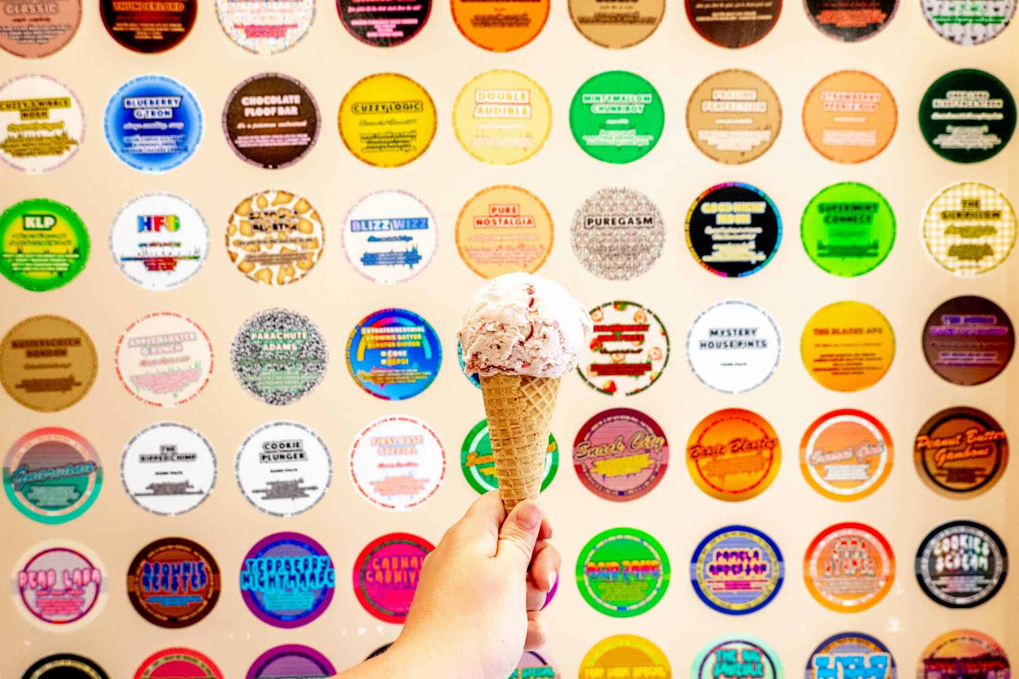 Hand holding ice cream cone in front of a wall covered with stickers