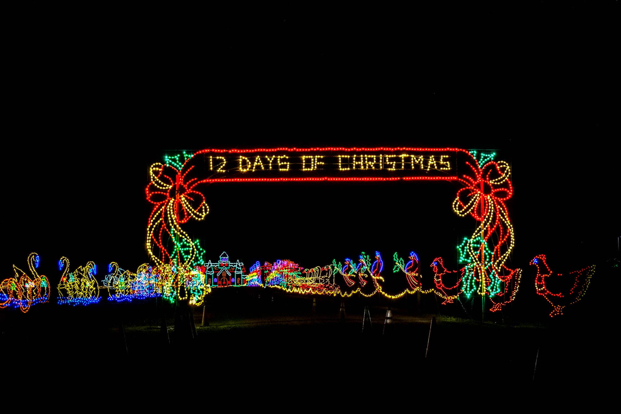 Illuminated sign for "12 Days of Christmas" in front of a light display.