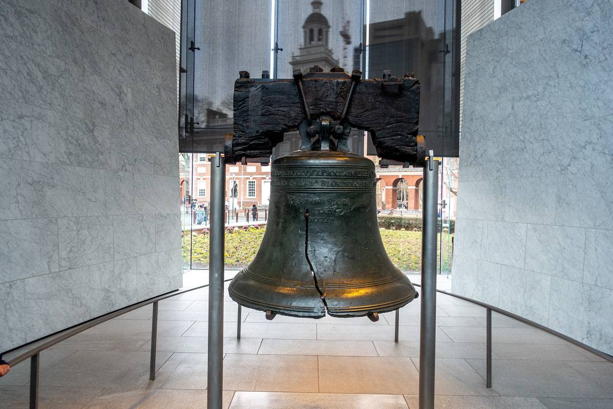 Large, cracked bell displayed in front of a window in a museum. 