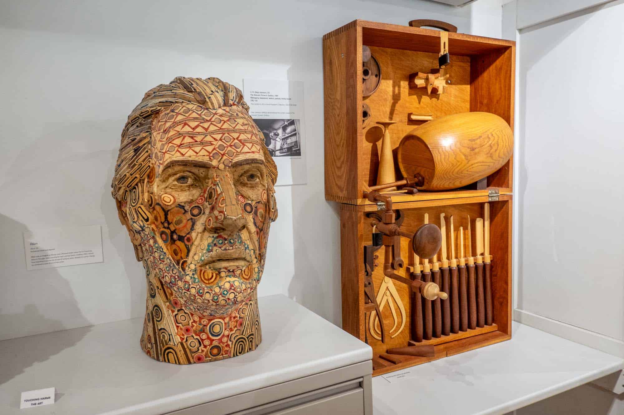Large wooden bust of a man's head with colorful lines of pigment embedded in it.