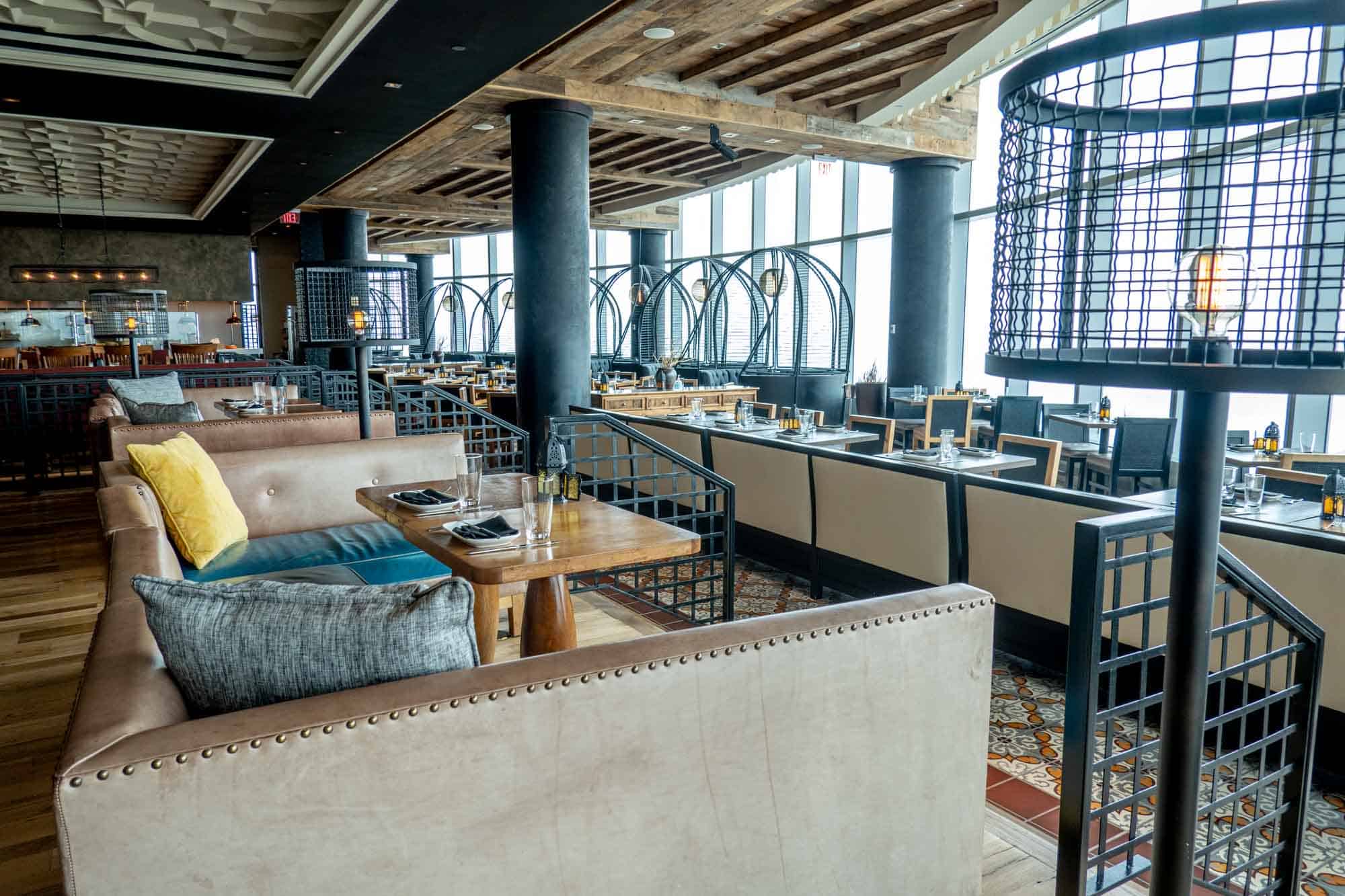 Tables and chairs in a restaurant with a wall of windows.