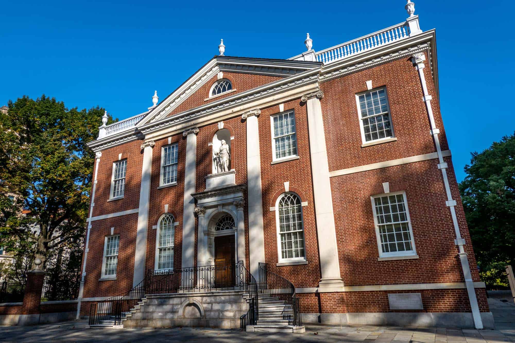 2-story brick building with rows of windows and a large statue of a man in a niche over the door.