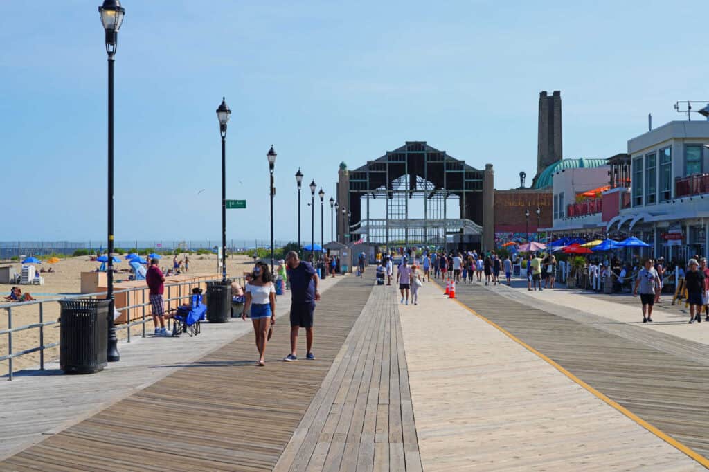 People walking on a boardwalk between the beach and shops