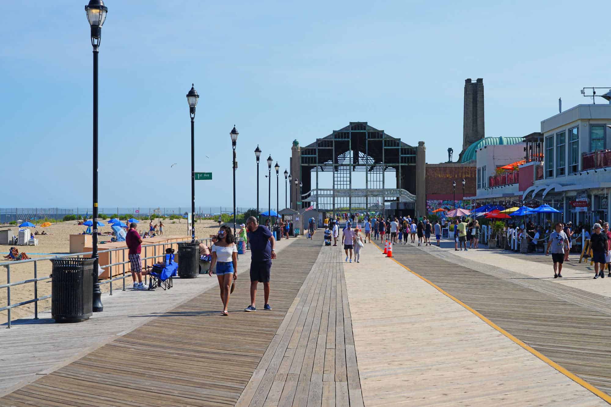 People walking on the Asbury Park Boardwalk between the beach and a row of shops