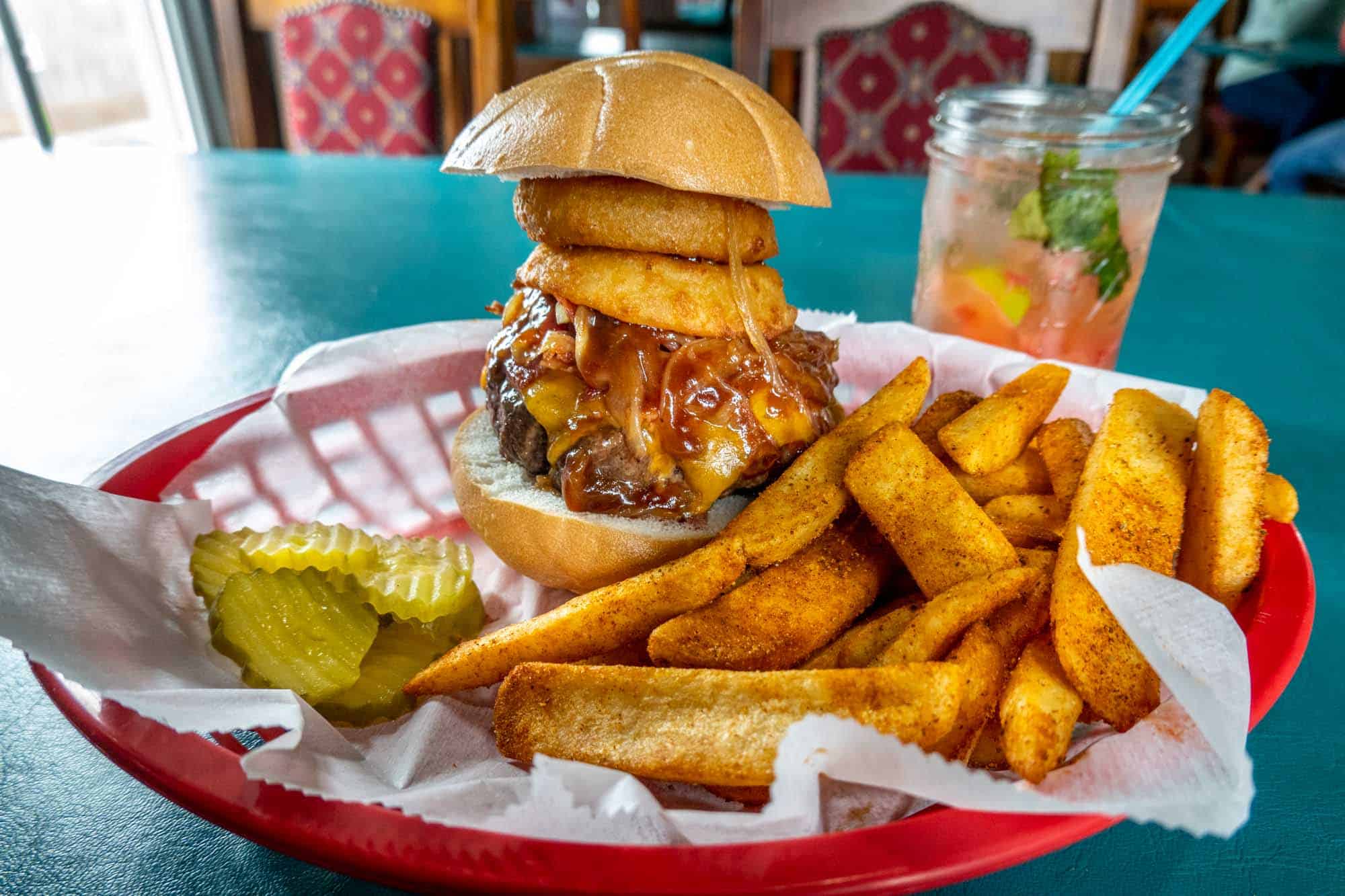 Basket of a hamburger and French fries beside a cocktail in a Mason jar.