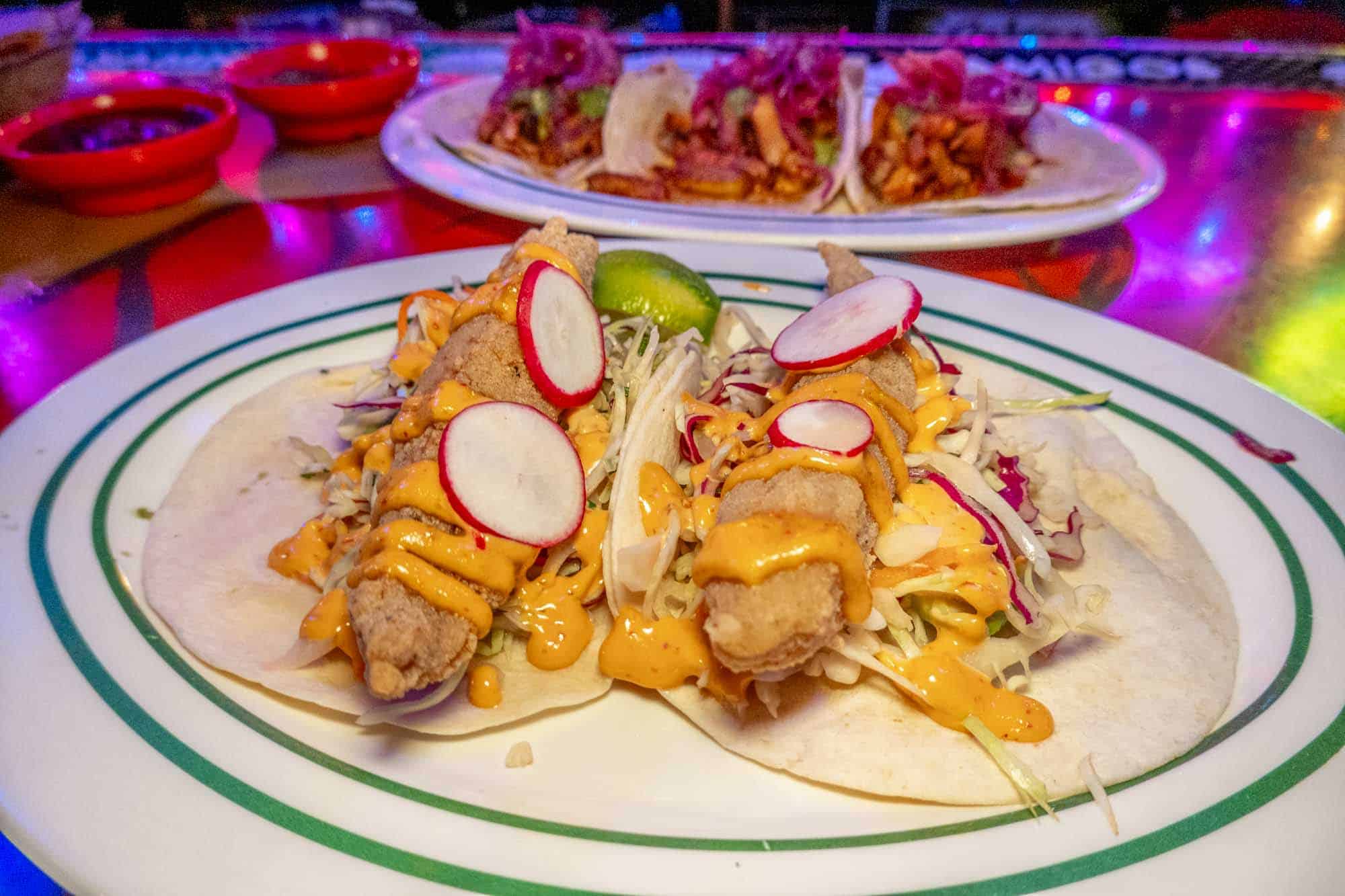 Two fish tacos topped with radishes on a plate.