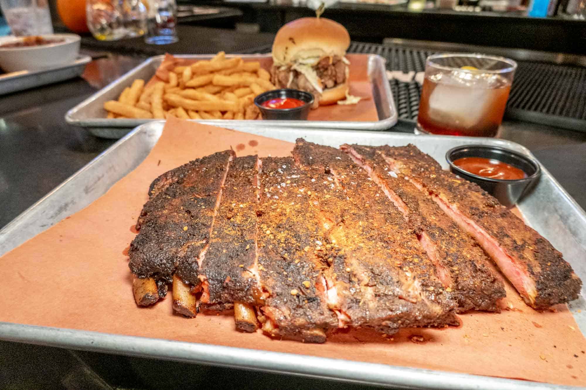 BBQ ribs on a tray in front of a tray with a sandwich and French fries