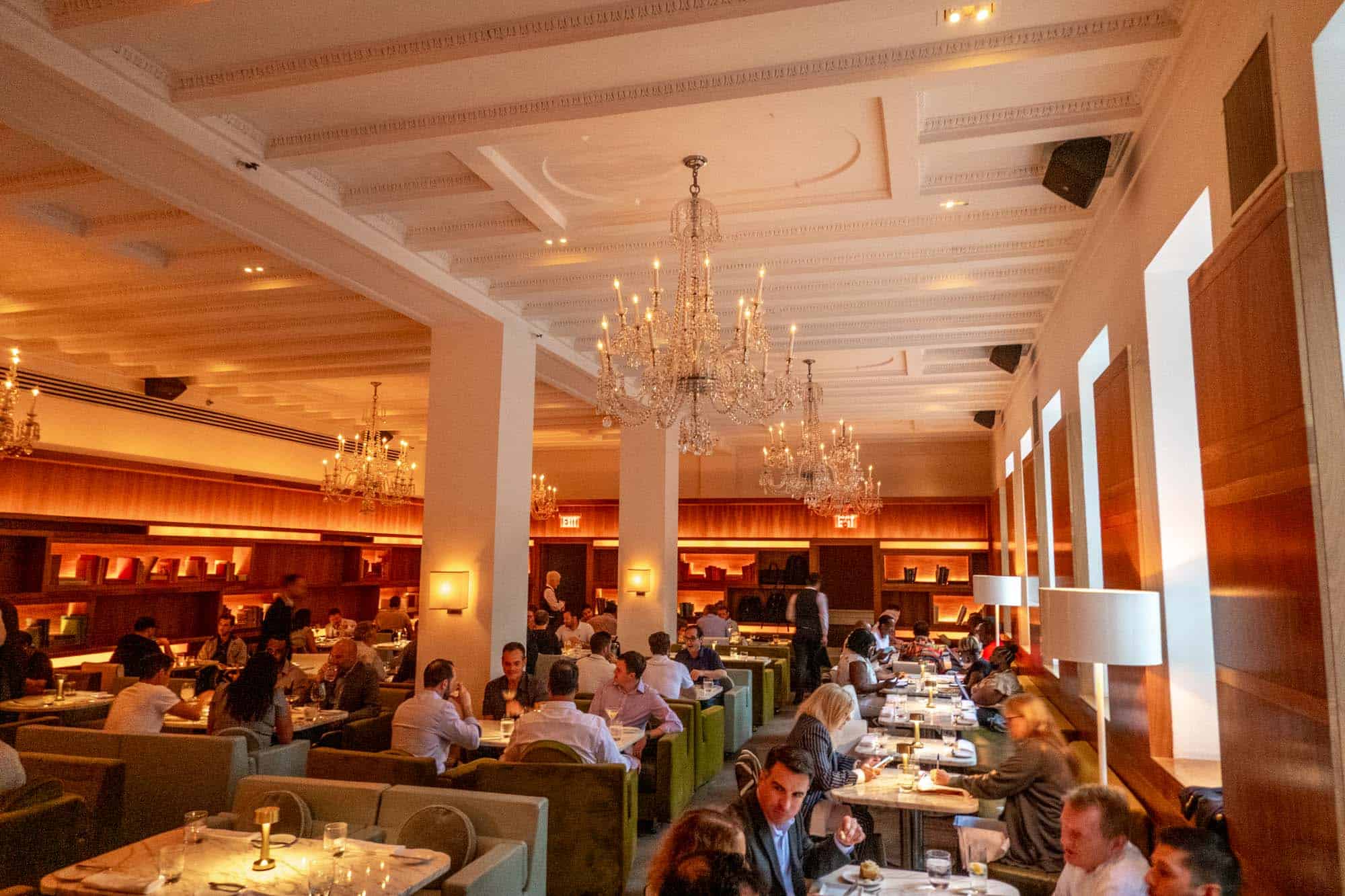 People in a restaurant dining room with green booths and large chandeliers. 