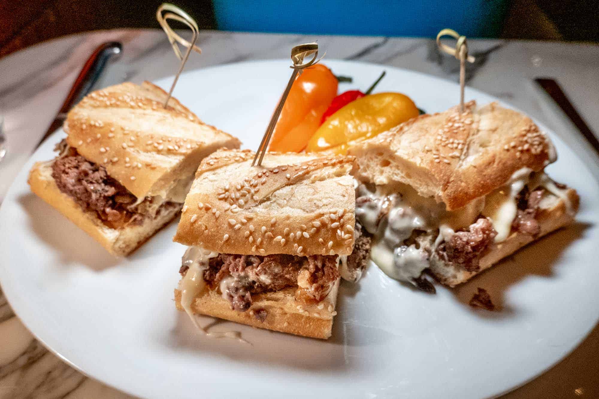 Cheesesteak on plate cut into three portions.