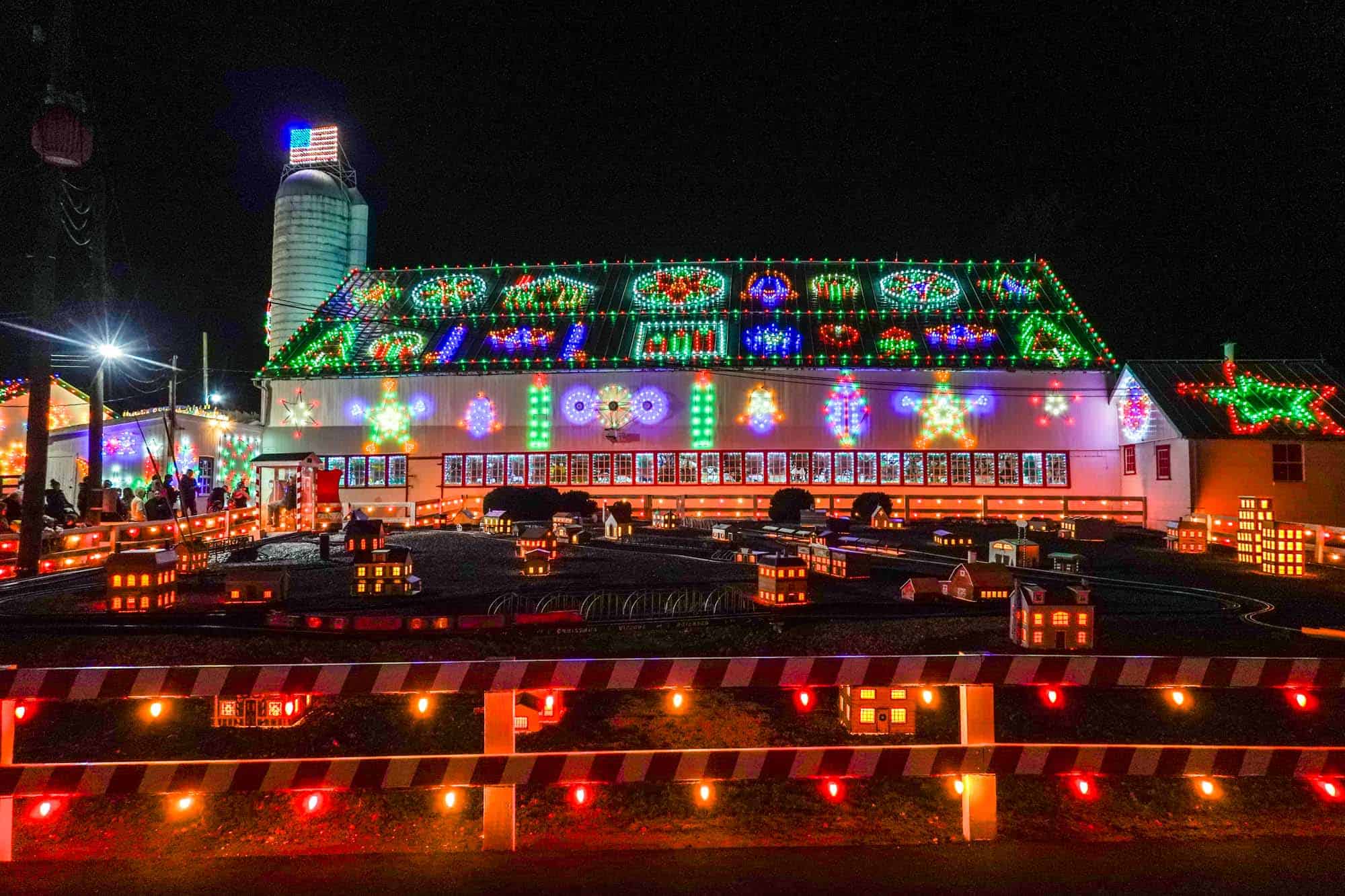 Barn at Koziar's Christmas Village decked out in lights with model railway in front