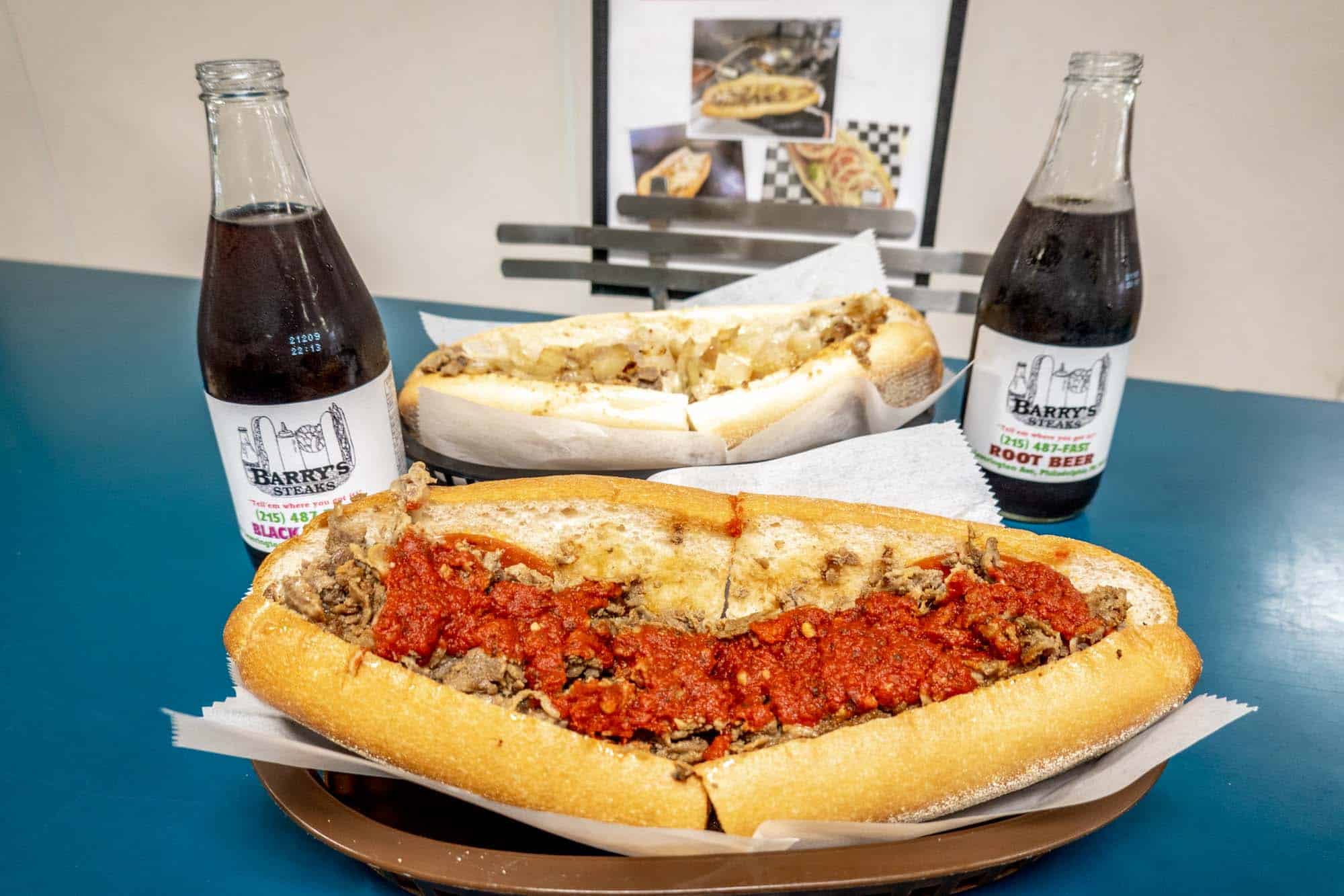 Two cheesesteaks and two soda bottles on a restaurant counter.