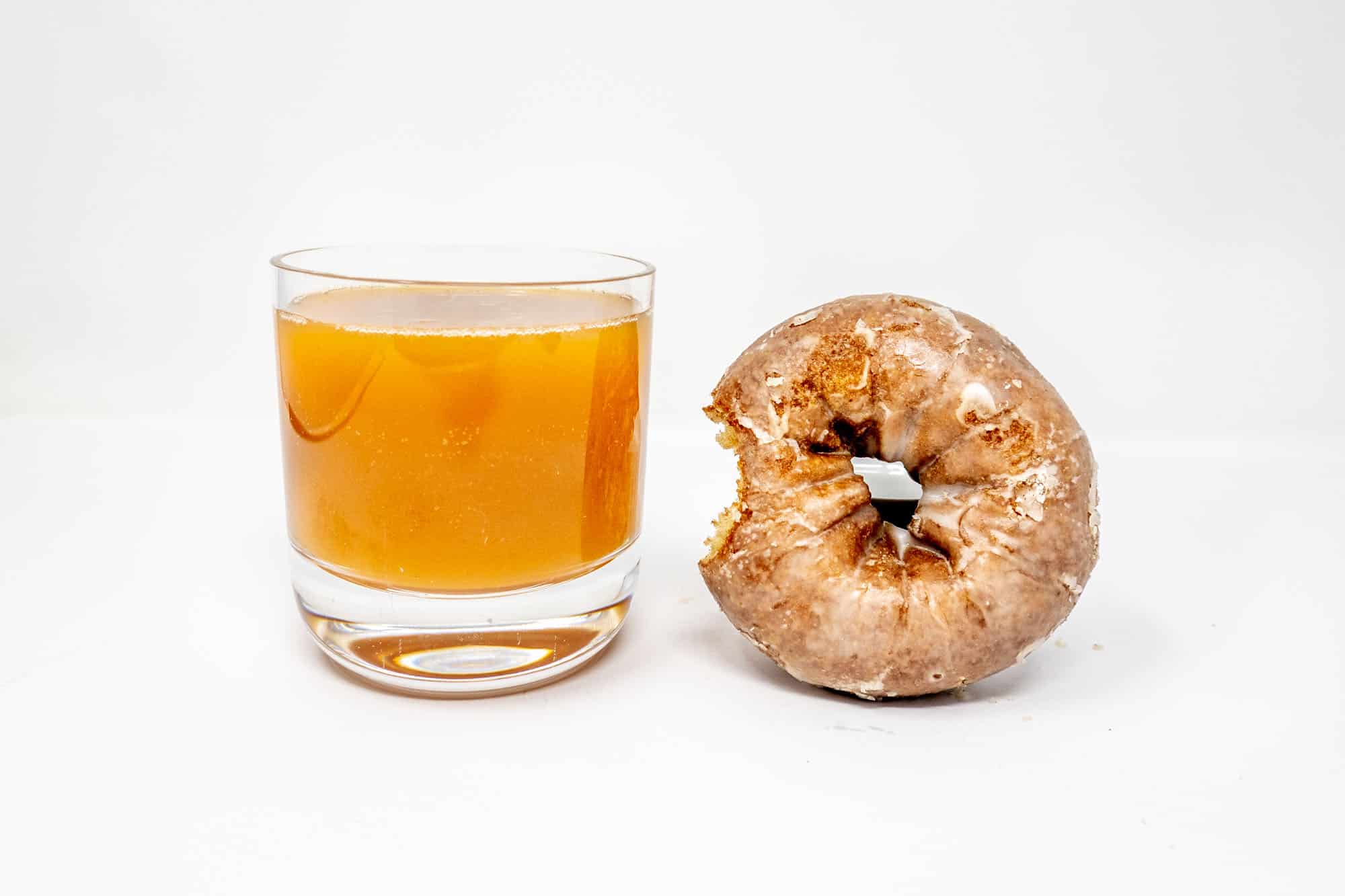 Glazed doughnut with a bite taken out beside a glass of apple cider
