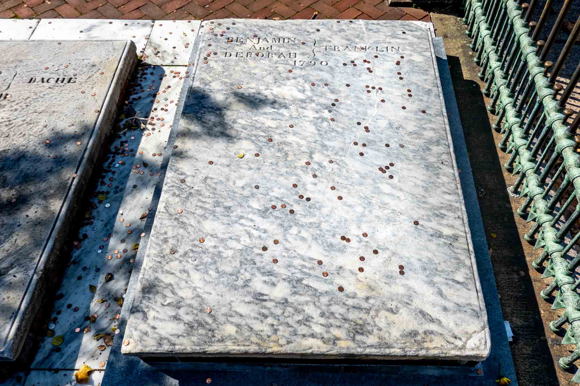 Marble slab grave marker inscribed with "Benjamin and Deborah Franklin, 1790" and covered with dozens of pennies