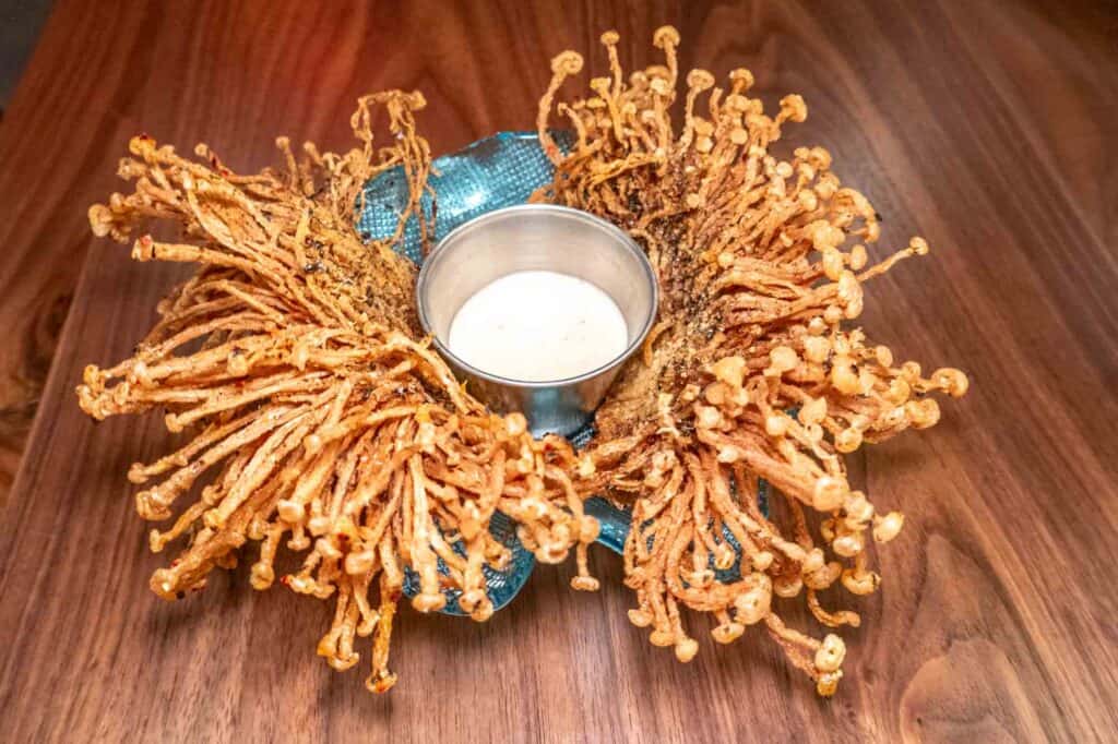 Fried enoki mushroom on a platter with sauce in the center.