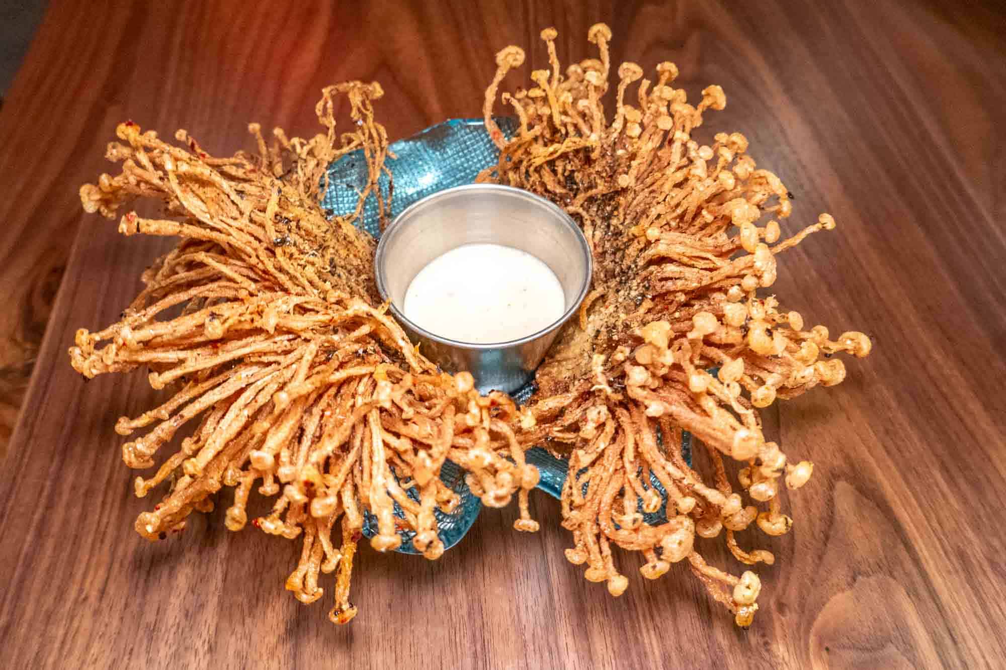 Fried enoki mushroom on a platter with a container of sauce.
