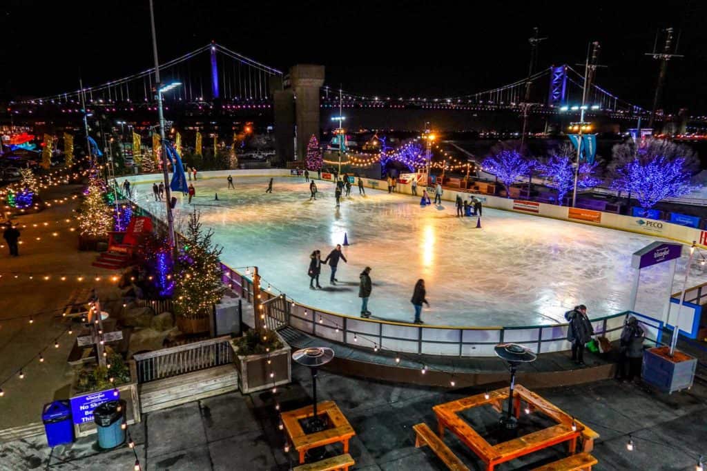Overhead view of skaters on an ice-skating rink surrounded by Christmas lights at night