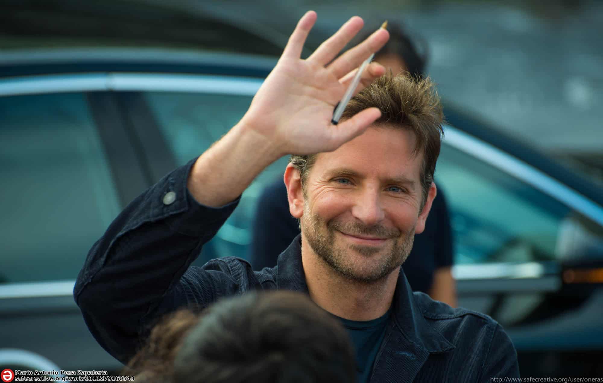 Bradley Cooper with pen in his hand waving to camera