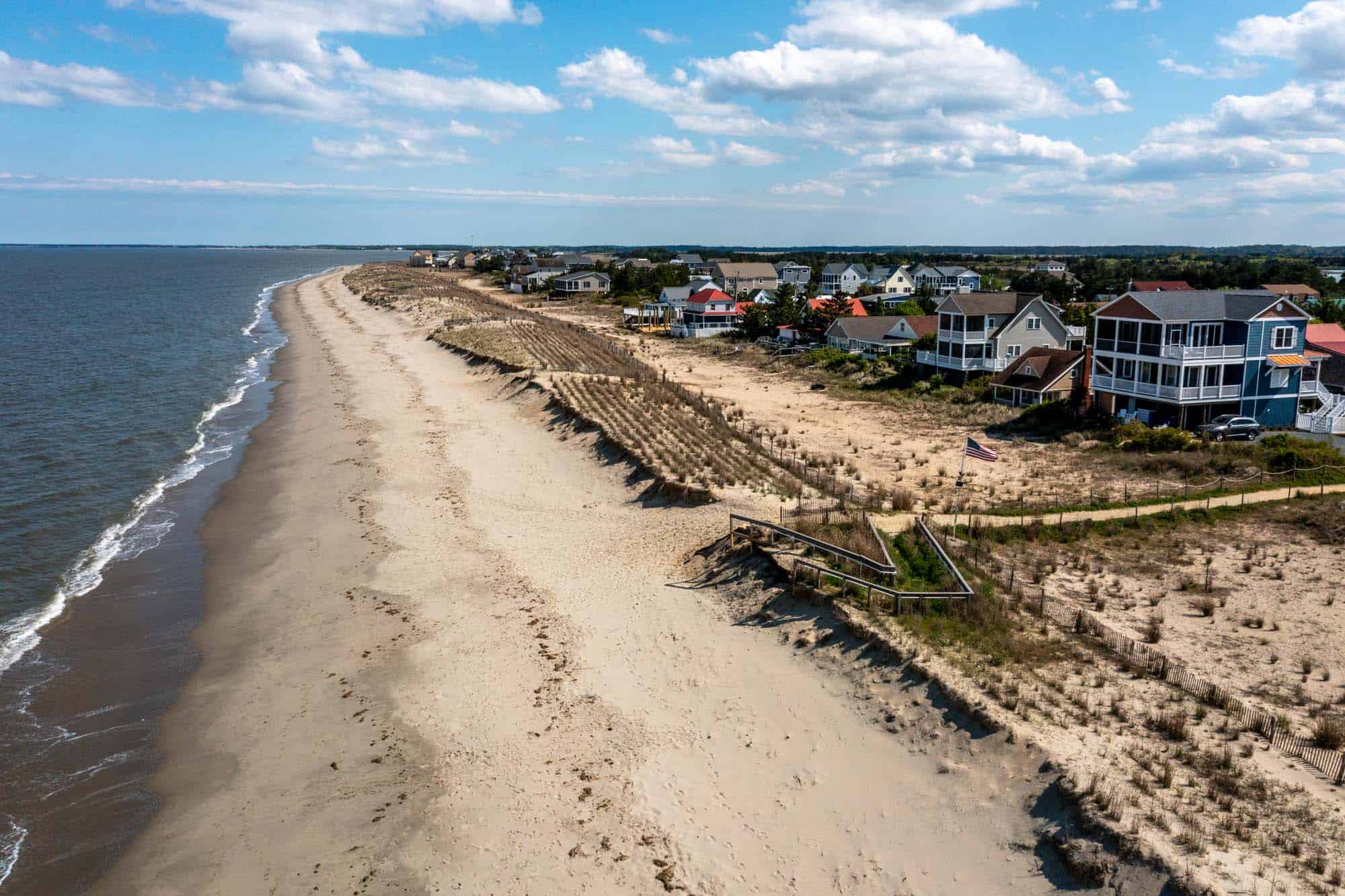 Ocean waves on a sandy beach with sea grass beside a row of homes.