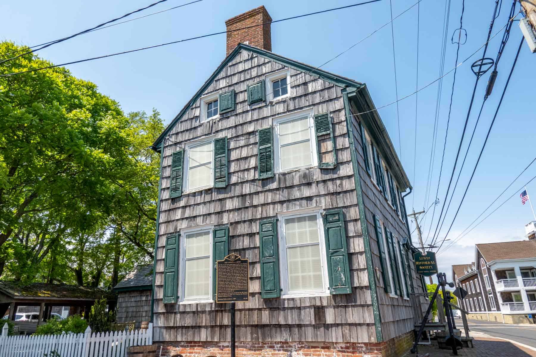 Wood shingled building with turquoise window shutters and a historical marker sign