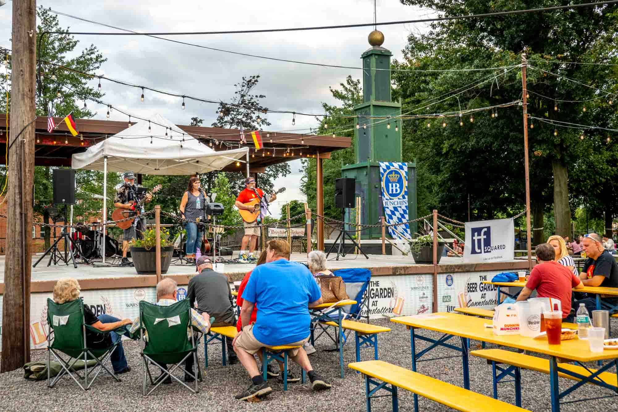 People watching musicians on a stage in a beer garden.