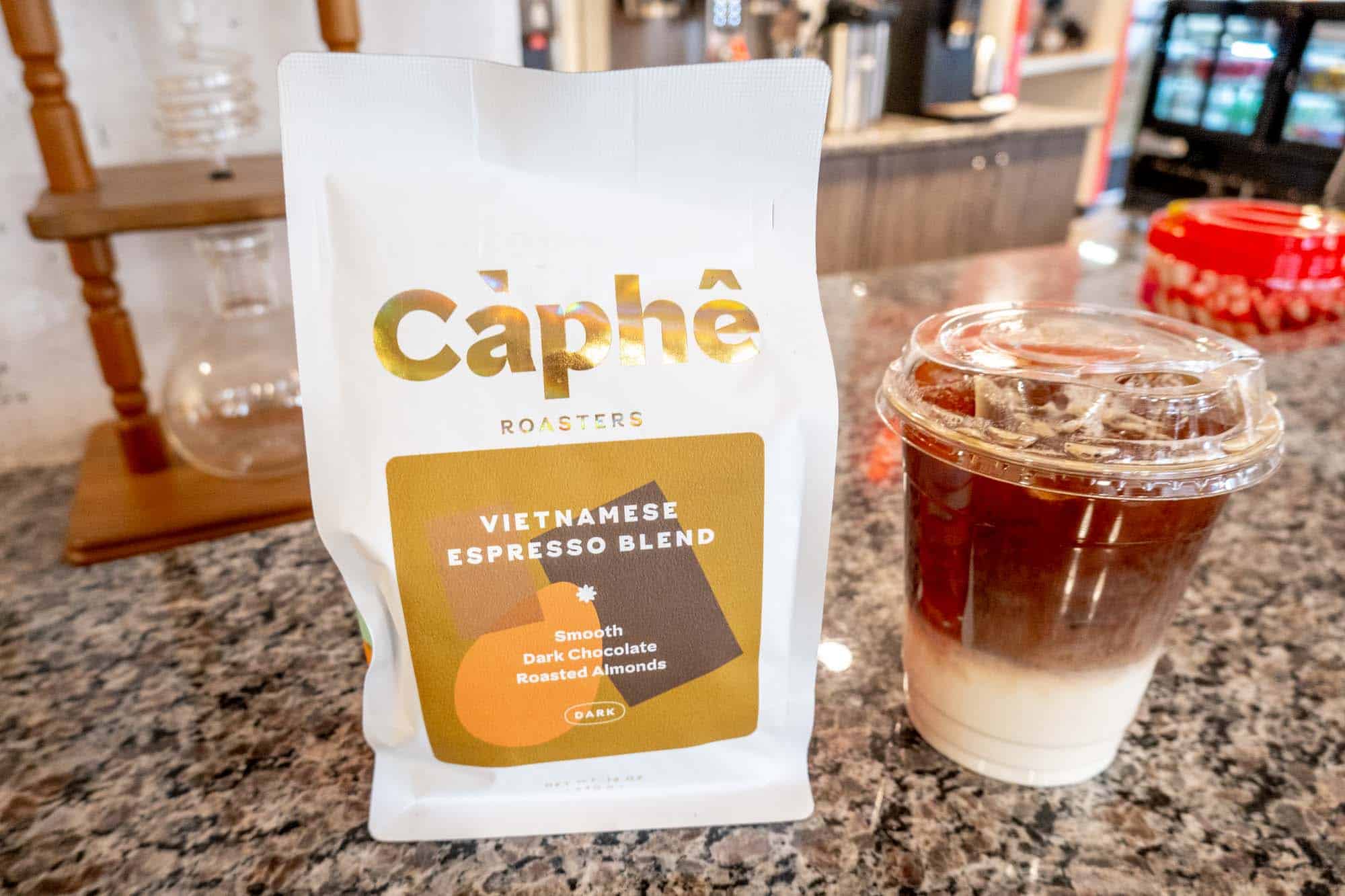 Bag of espresso coffee on a counter next to a coffee with a layer of milk at the bottom.