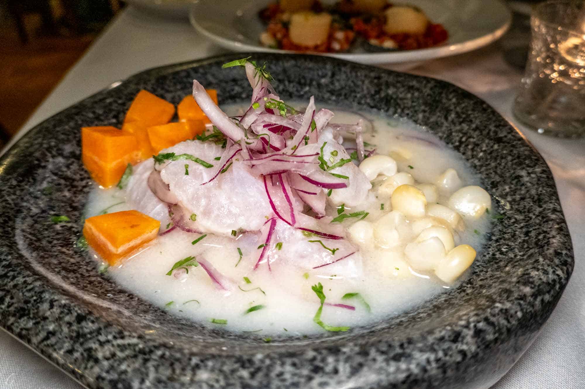 Stone bowl filled with ceviche, including fish, corn, red onion, and sweet potato.