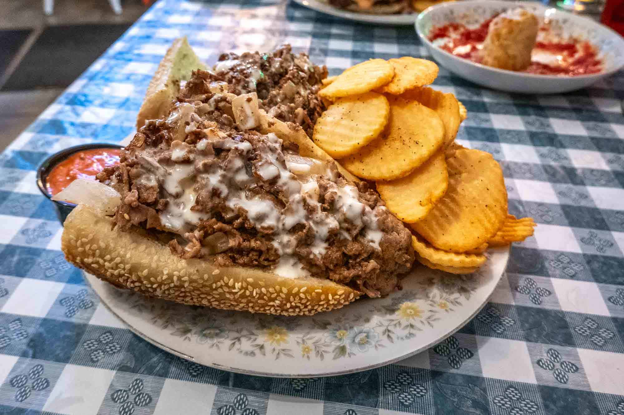 Cheesesteak sandwich and fried potatoes on a restaurant table.
