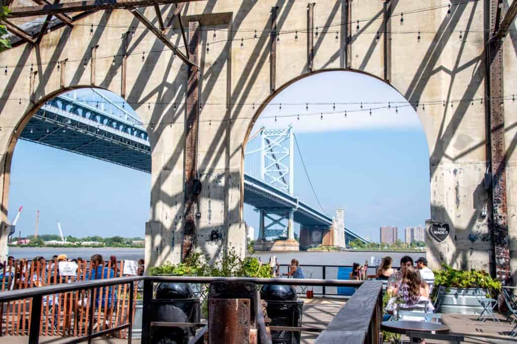 People at tables on Cheery Street Pier with Benjamin Franklin Bridge in background