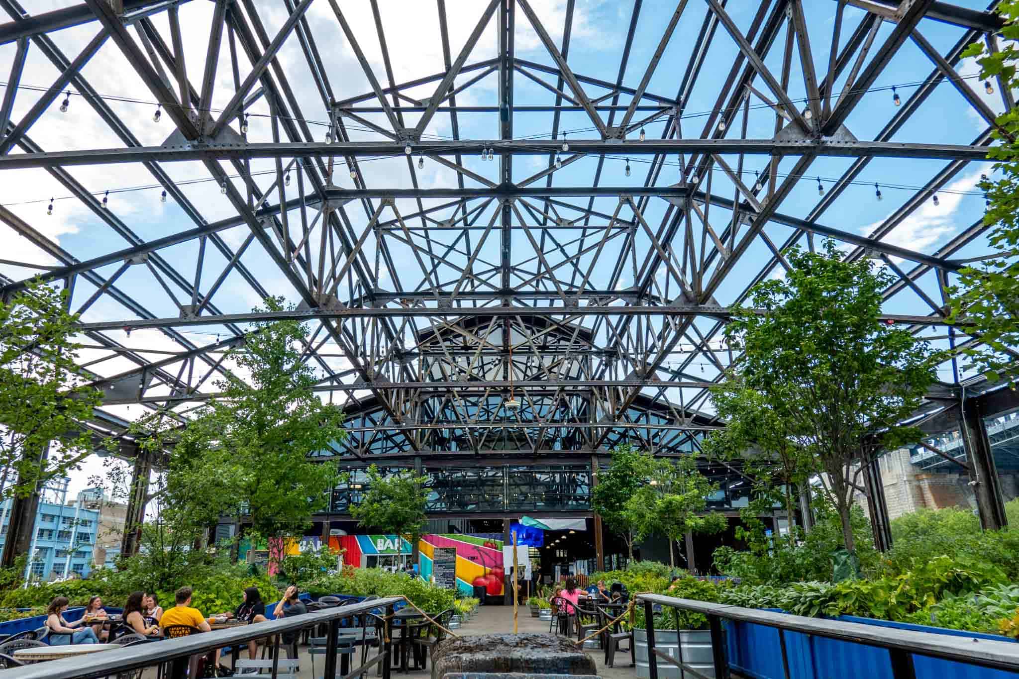 People sitting at tables under the iron framework of an old pier.