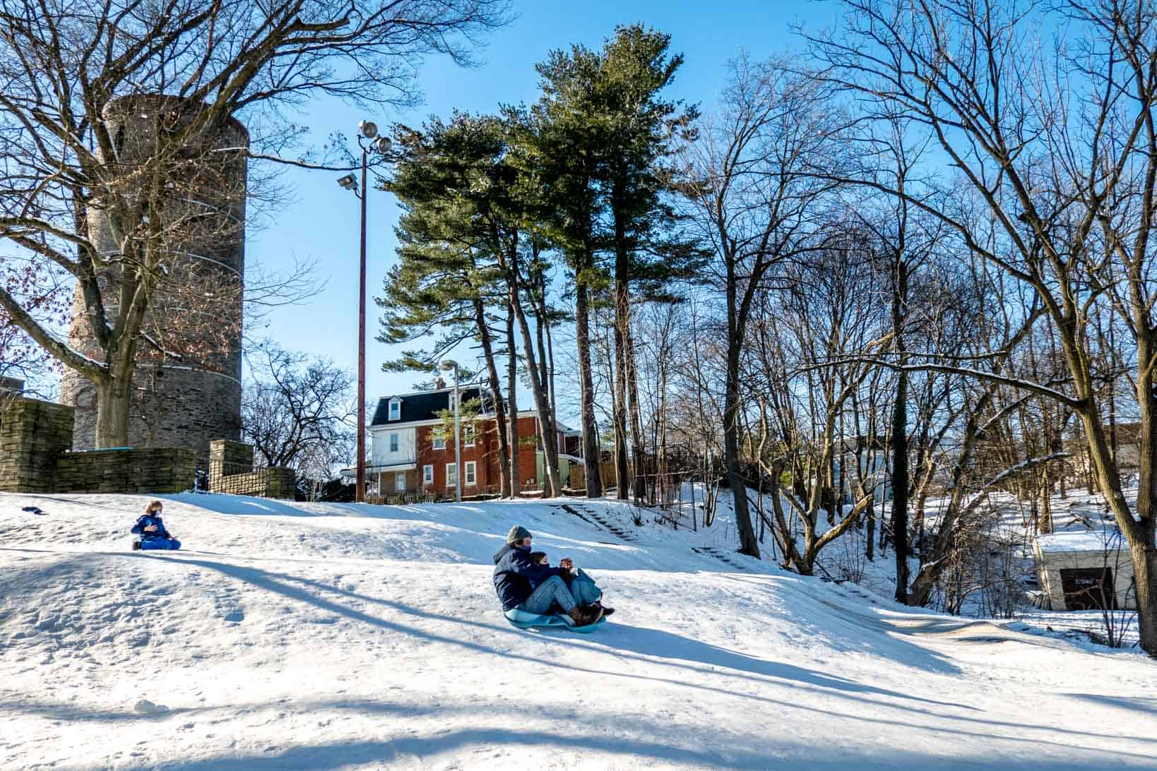 People sledding on a hill with a tall stone tower in the background