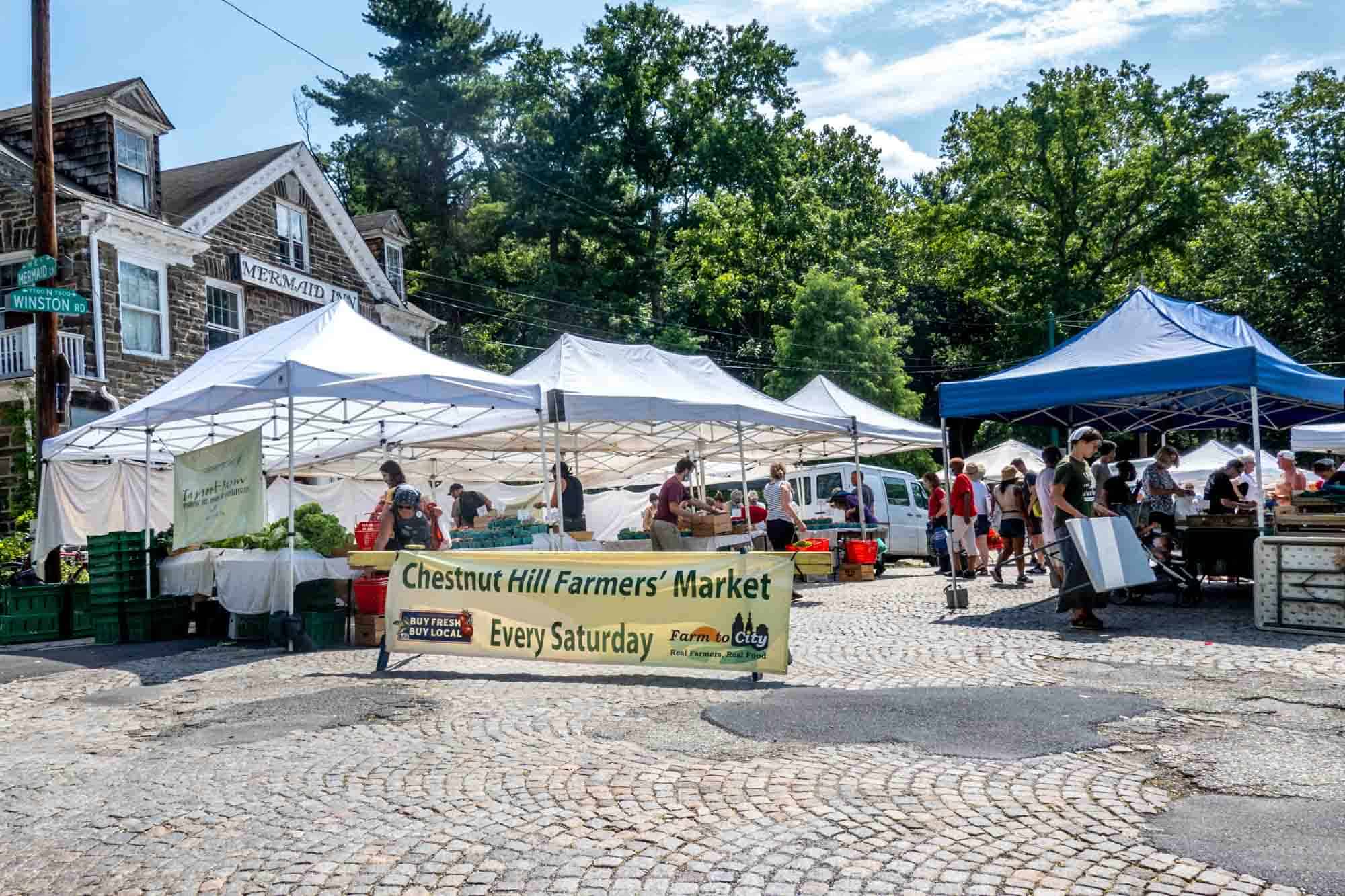 Tents by sign reading "Chestnut Hill Farmers' Market Every Saturday"