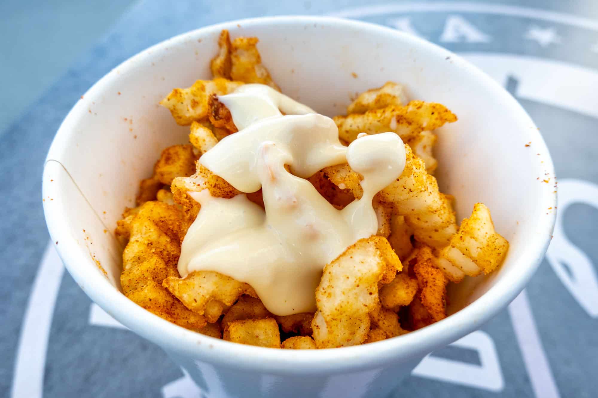 Crinkle French fries covered with spices and cheese sauce in a cup.