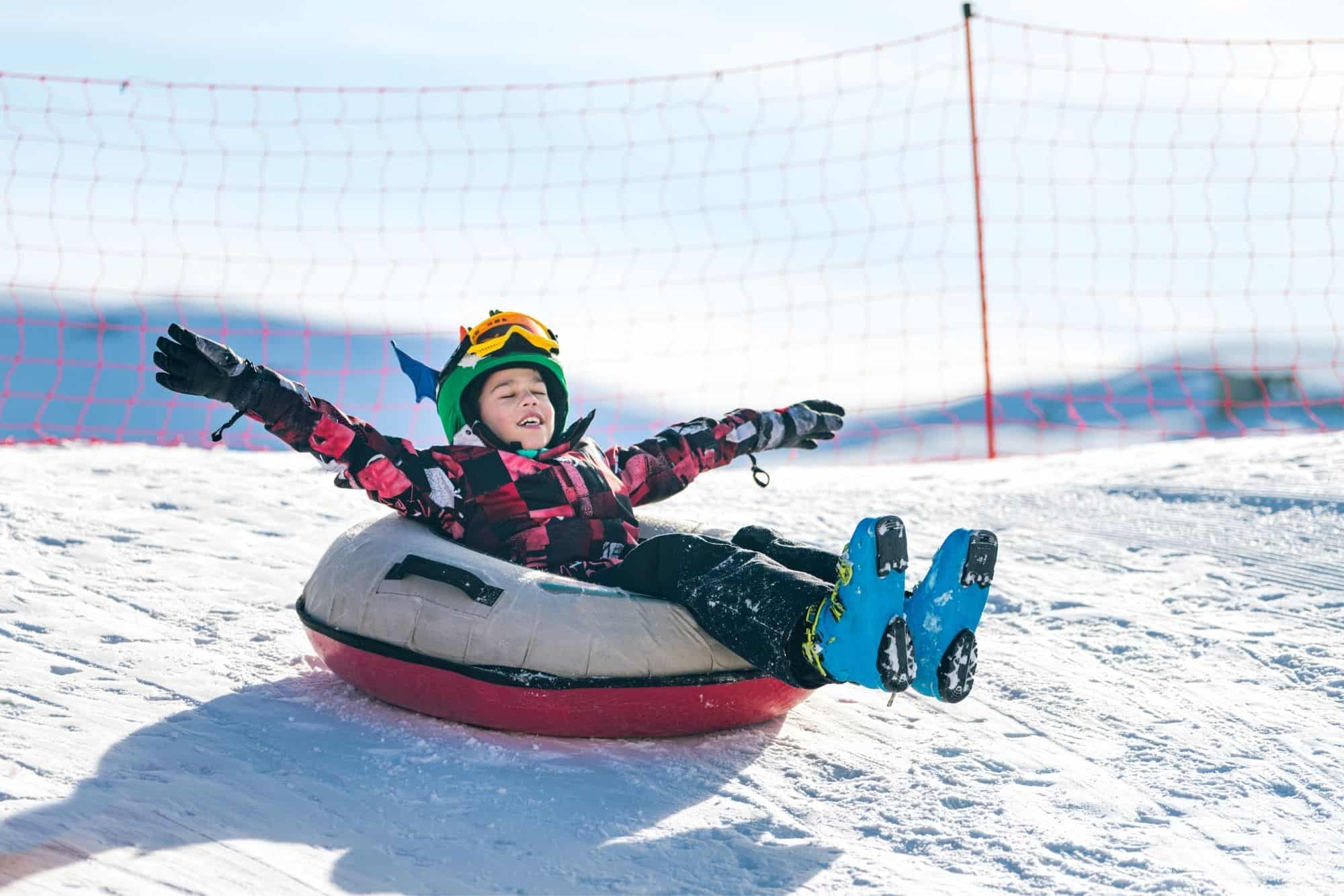 Child in ski clothes and ski boots riding snow tube
