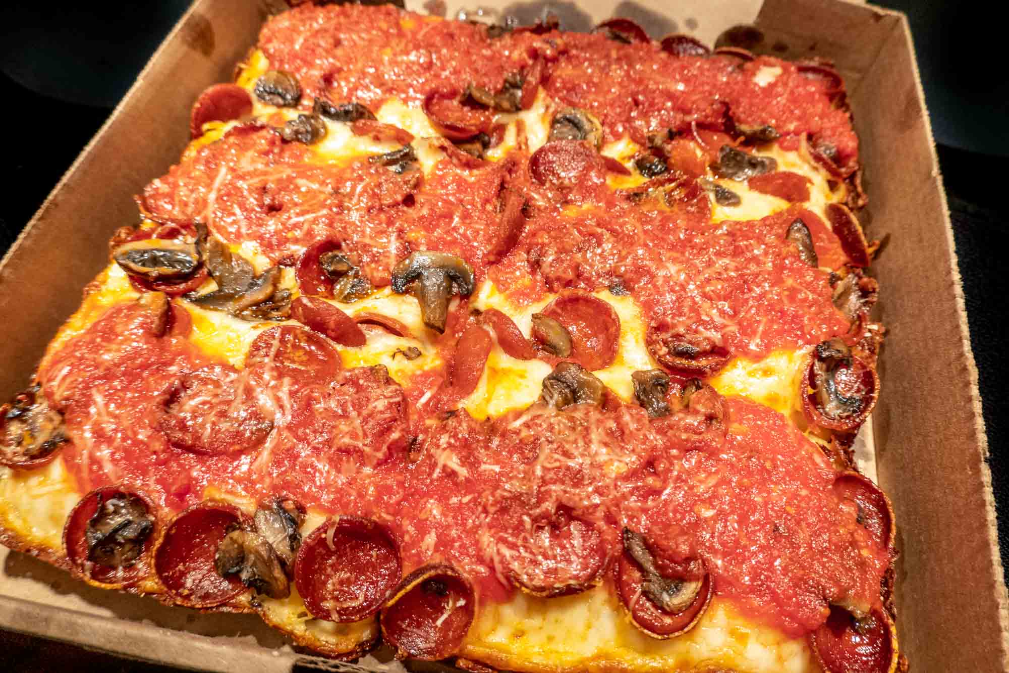 Pepperoni and mushroom pizza in brown cardboard box.