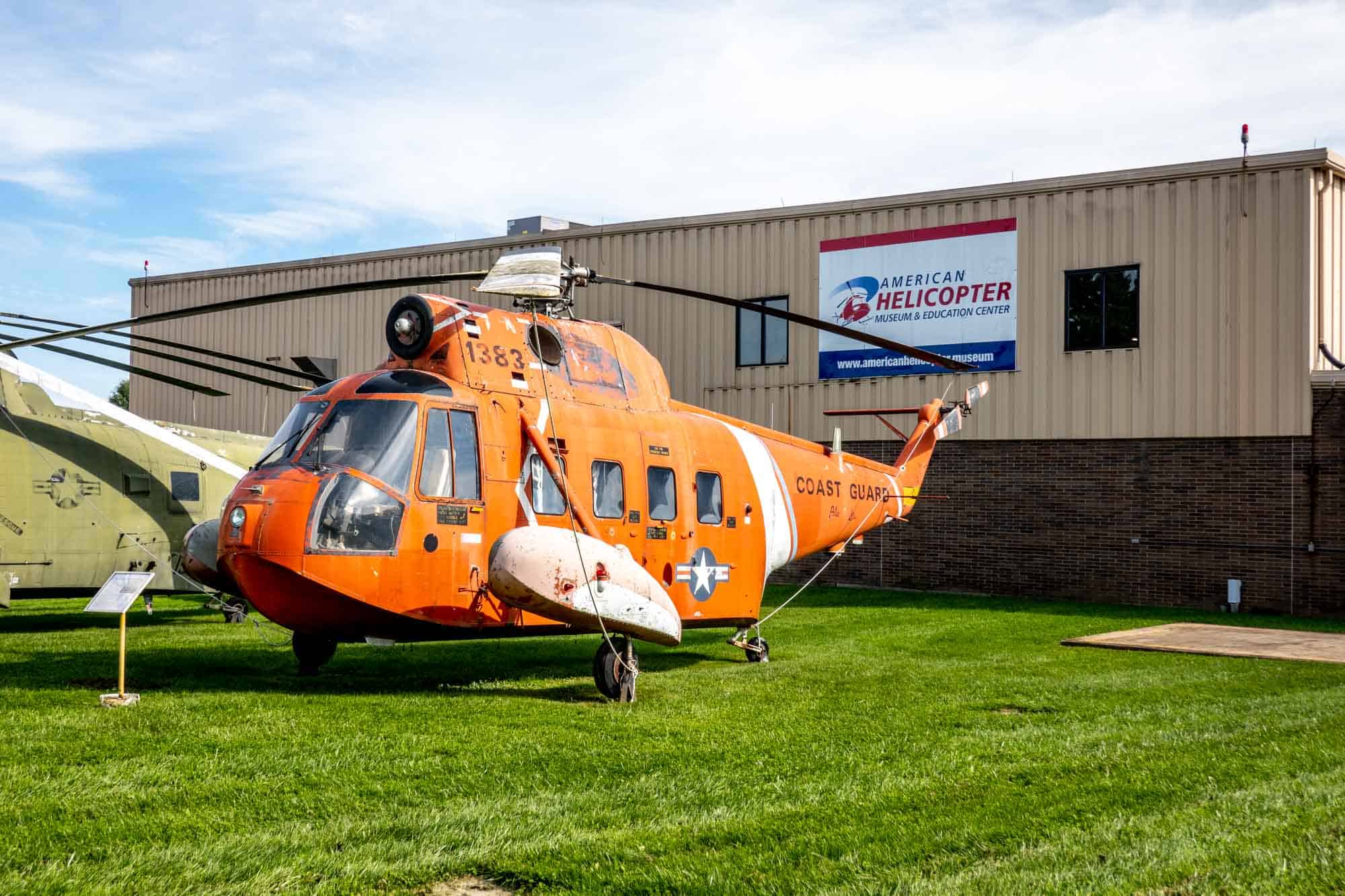 Orange Coast Guard helicopter displayed outside a building with signage for "American Helicopter Museum & Education Center"