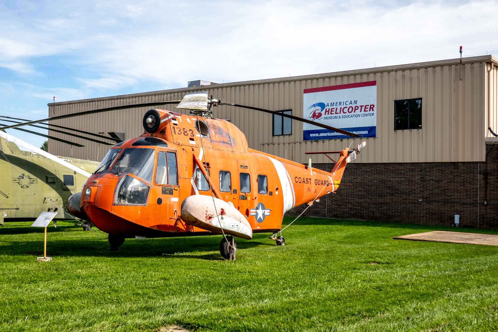 Orange Coast Guard helicopter displayed outside a building with signage for "American Helicopter Museum & Education Center."