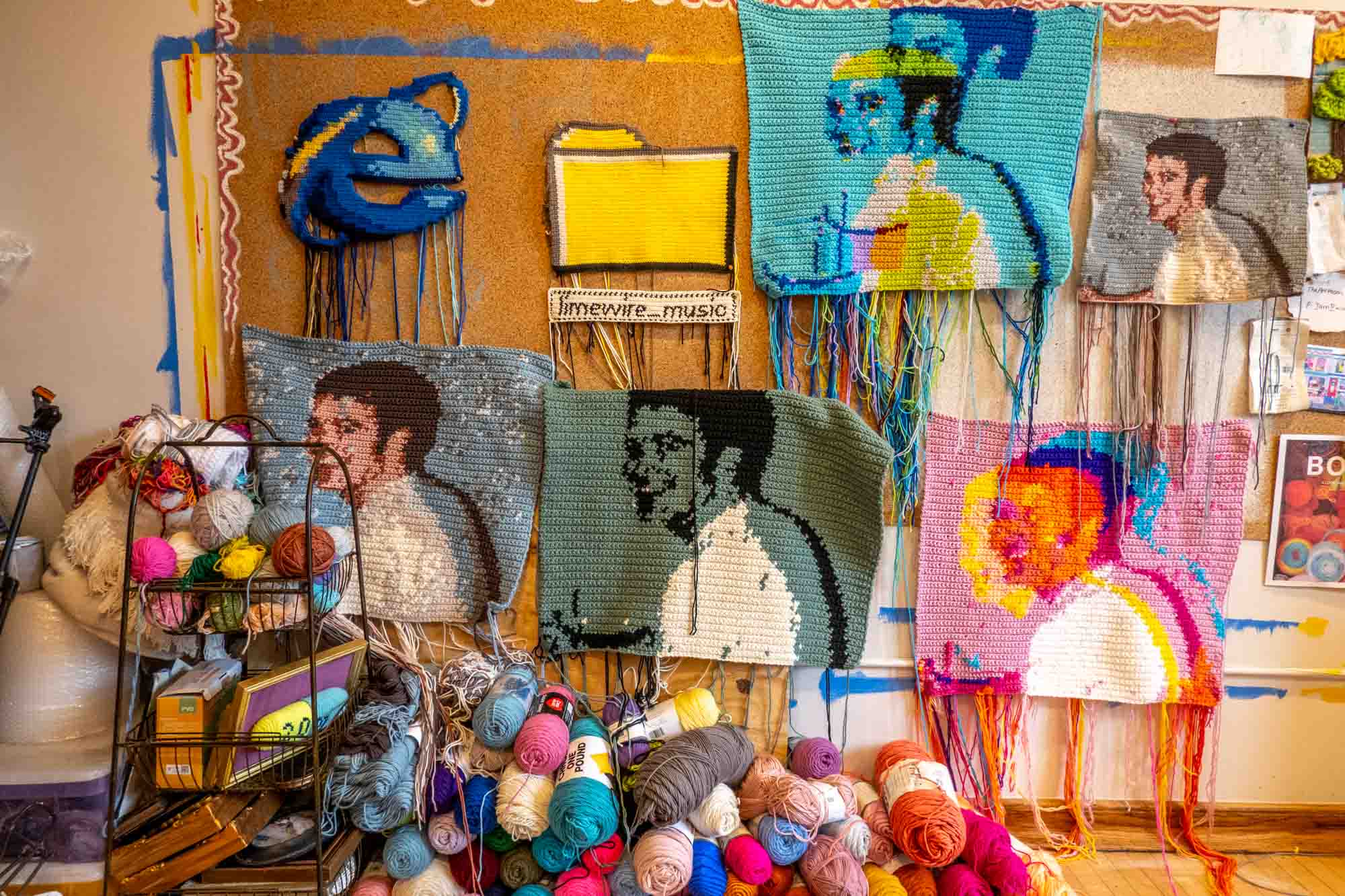 Large crochet squares featuring a man's head hanging on a wall above a pile of yarn.