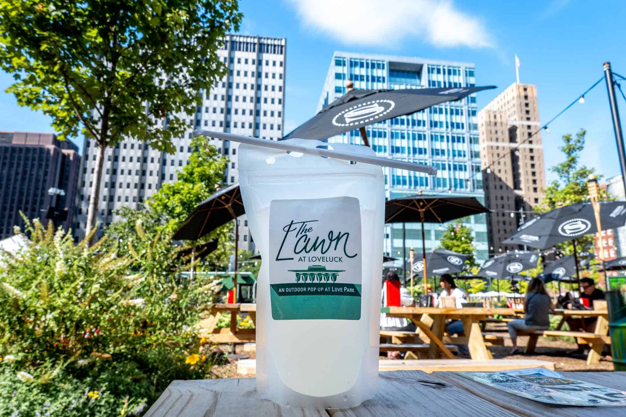 Cocktail pouch on picnic table reading "The Lawn at LoveLuck, an outdoor pop up at Love Park"