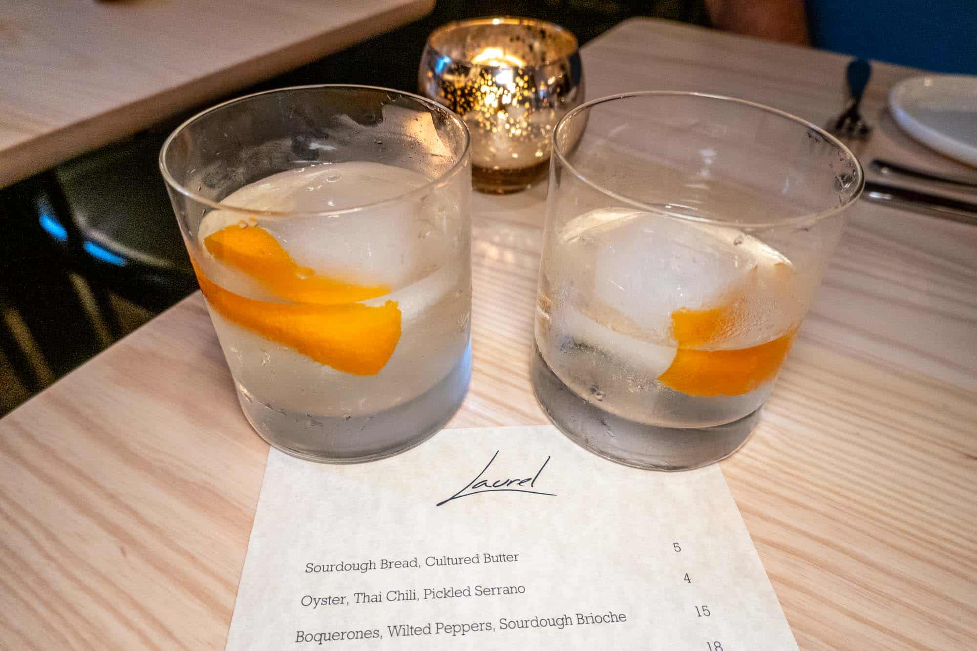 Cocktails with orange peel on table with menu that says "Laurel"