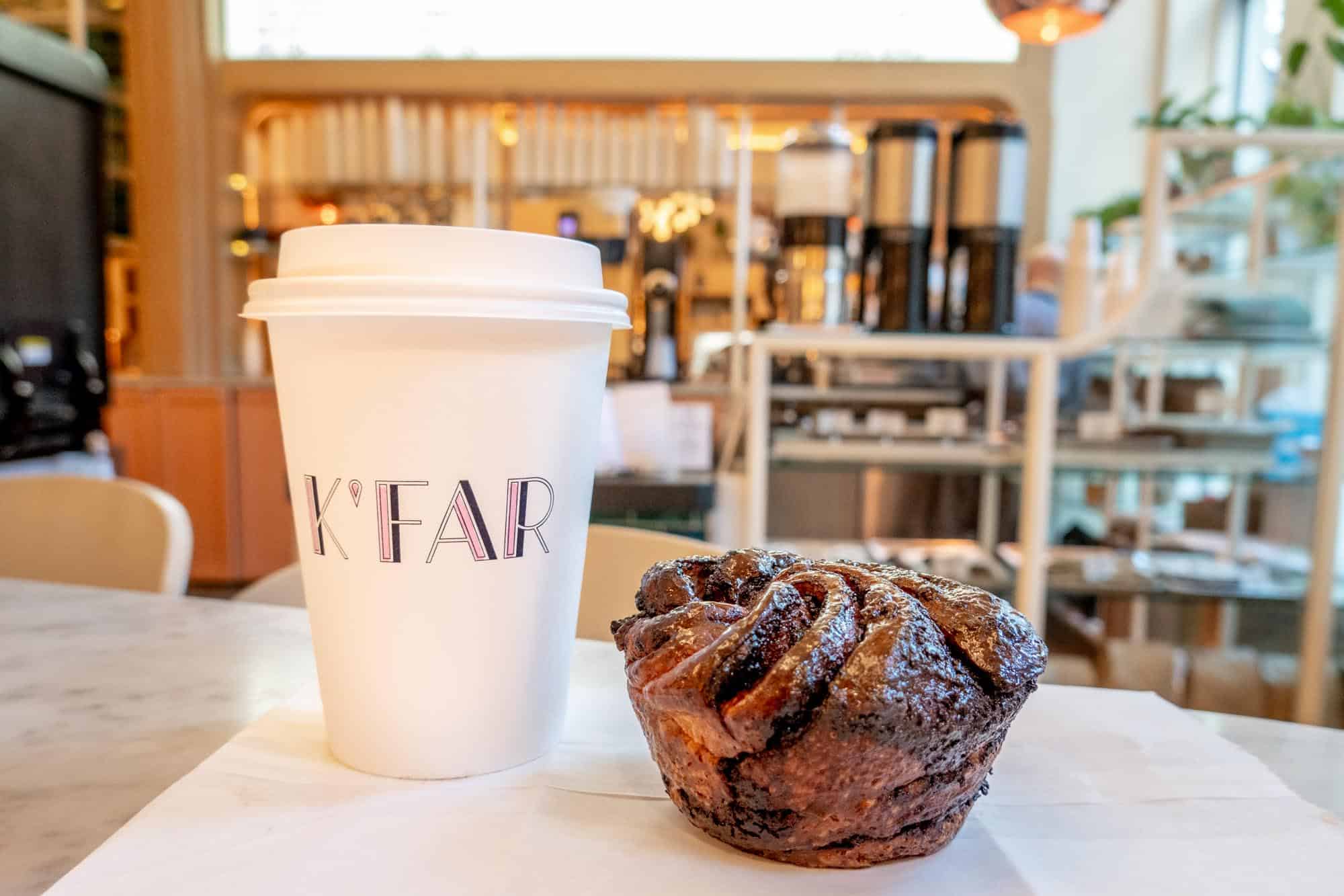 Coffee cup labeled "K'Far" and pastry on the counter in a cafe.