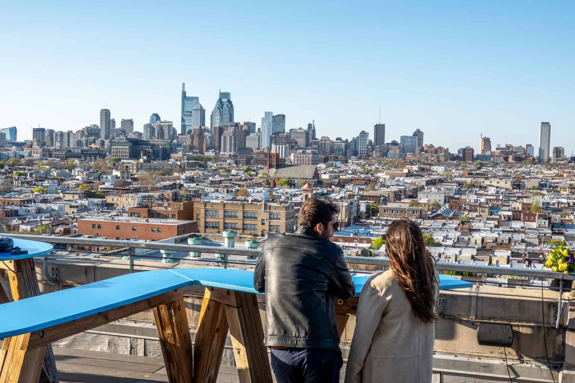 People standing at a rooftop bar with a view of the city skyline.
