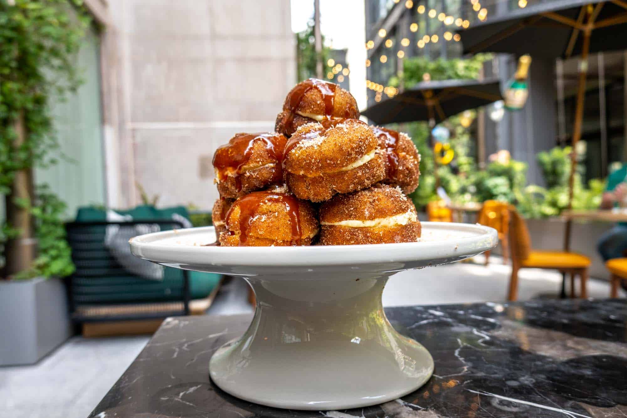 Pile of cinnamon-sugar-covered donuts on a platter on an outside table.