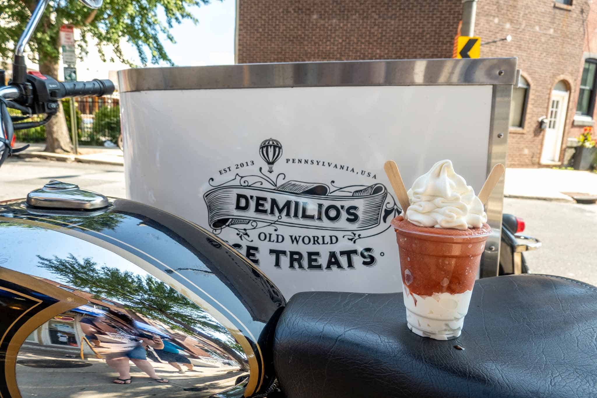 Cup filled with vanilla ice cream and birch beer water ice beside sign: "D'Emilio's Old World Ice Treats."