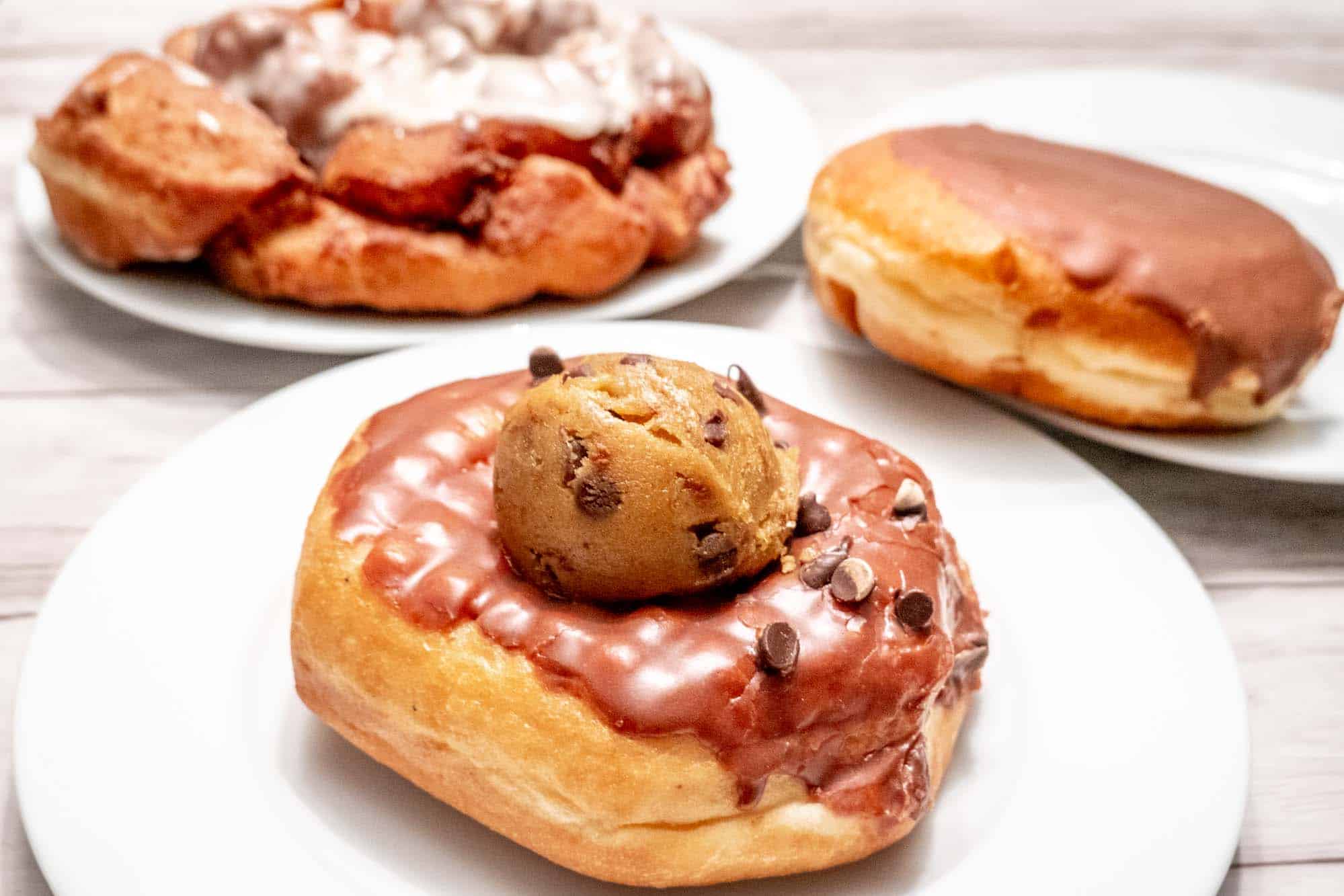 A fritter, a filled donut, and a donut topped with cookie dough on three plates.