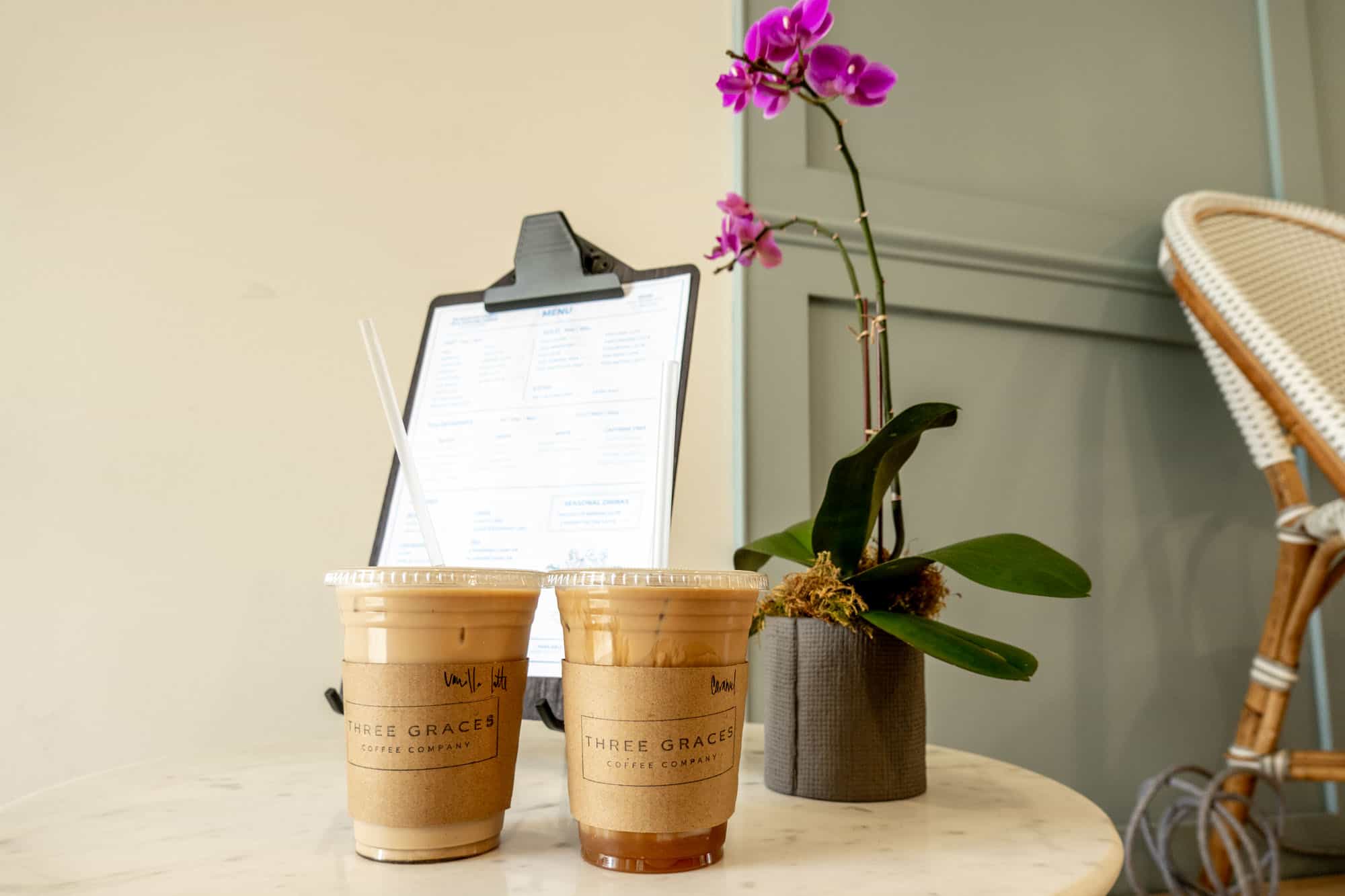 Two plastic cups of ice coffee on a table with sleeves labeled for "Three Graces Coffee Co."