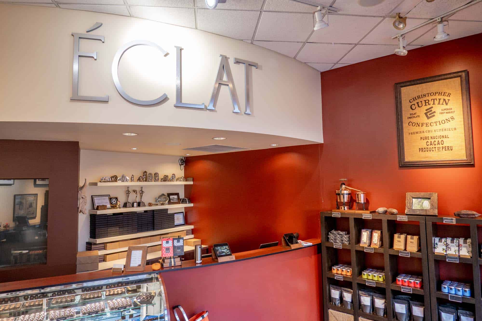 Interior of a chocolate store with red walls and a large silver sign: "Eclat."