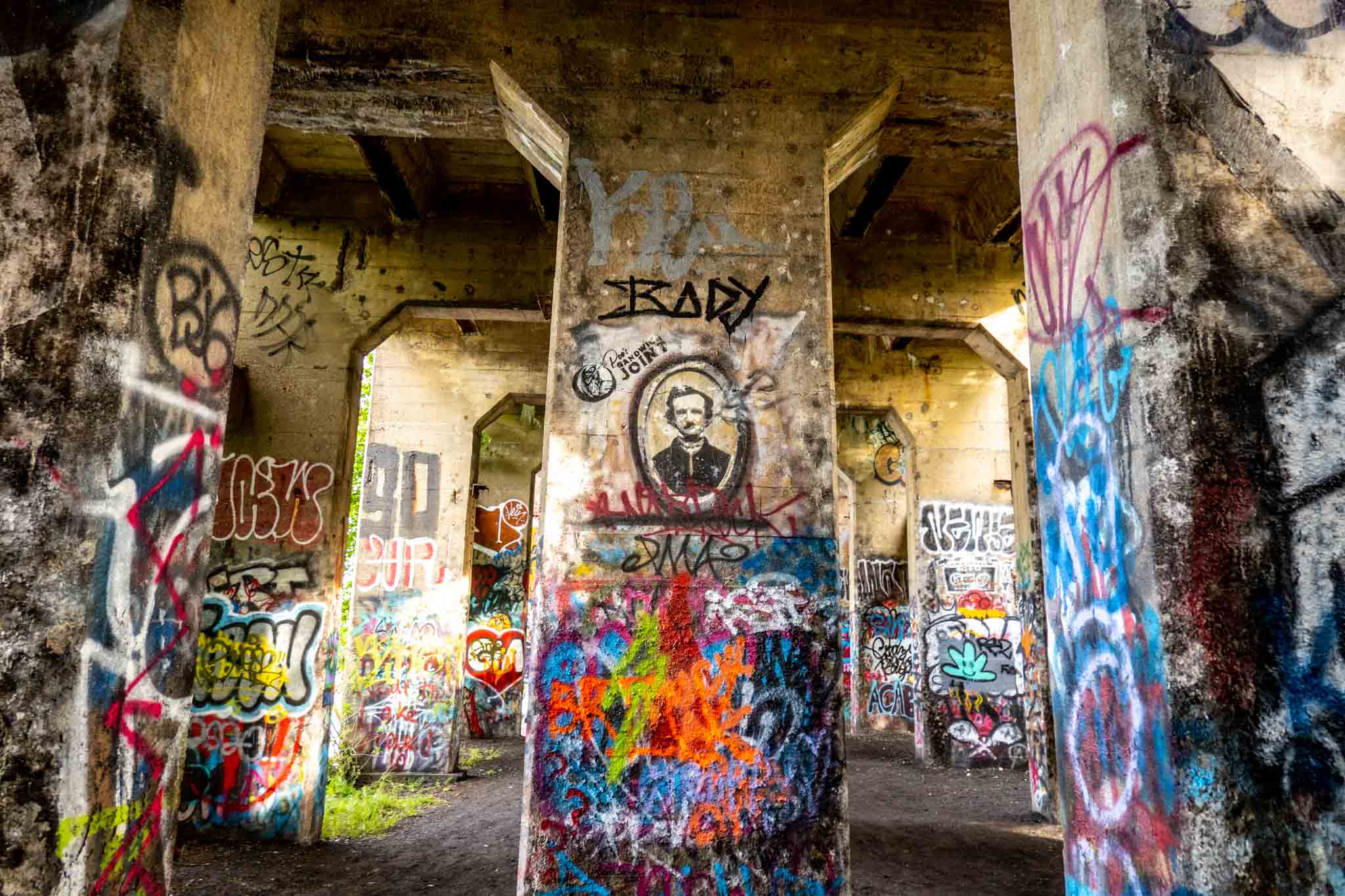 Concrete structure covered with graffiti and a spray painted portrait of a man.