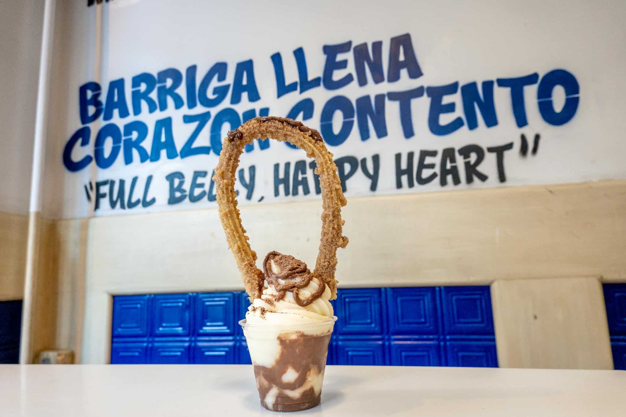 Cup of soft serve ice cream topped with a large churro bent into a circle.