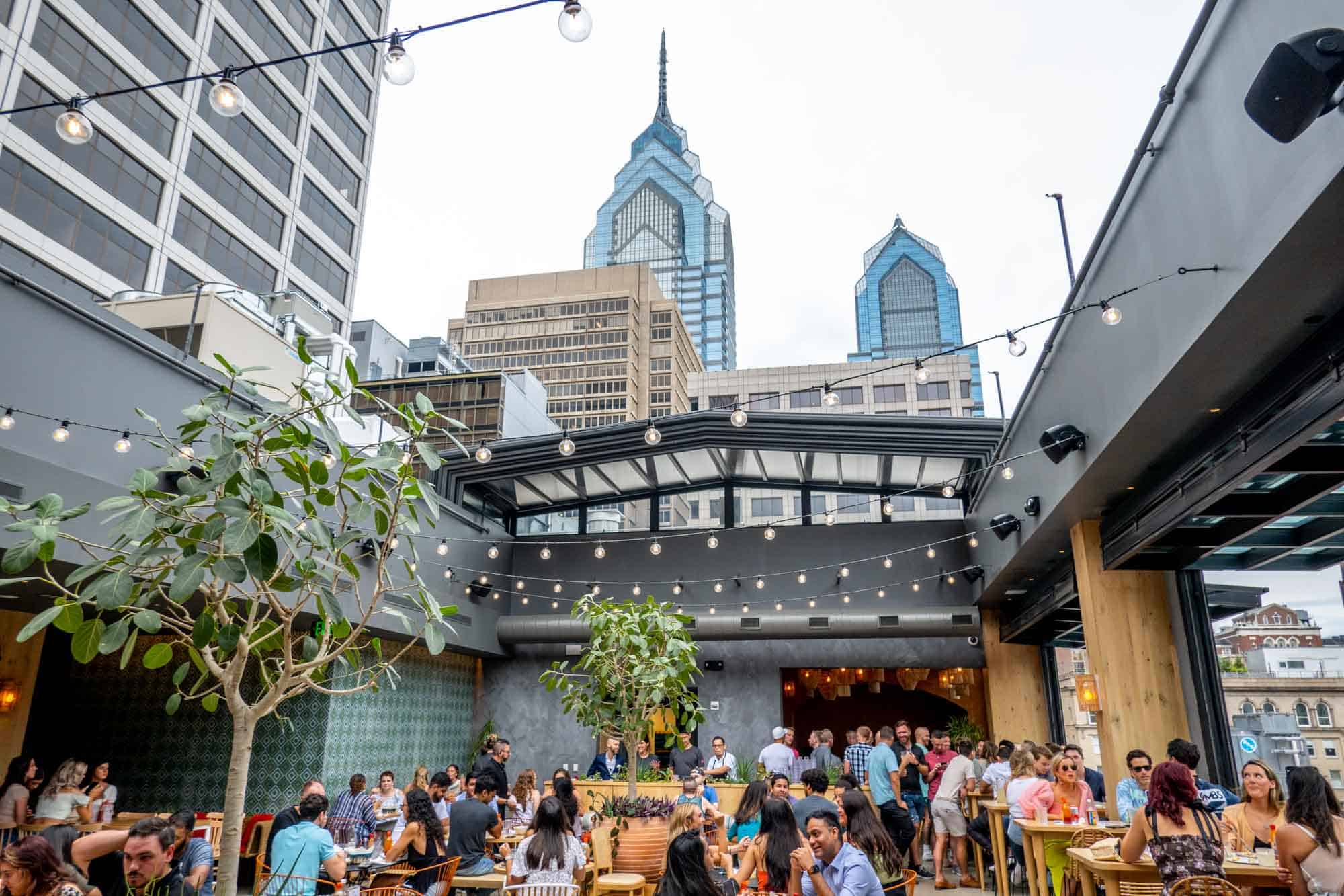 People at a rooftop restaurant with a view of skyscrapers.