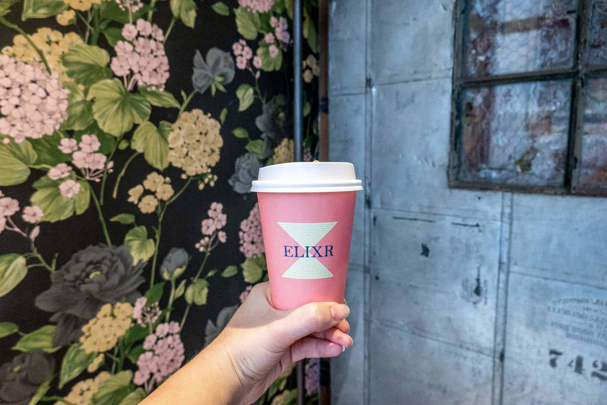Hand holding a pink coffee cup labeled "Elixr"